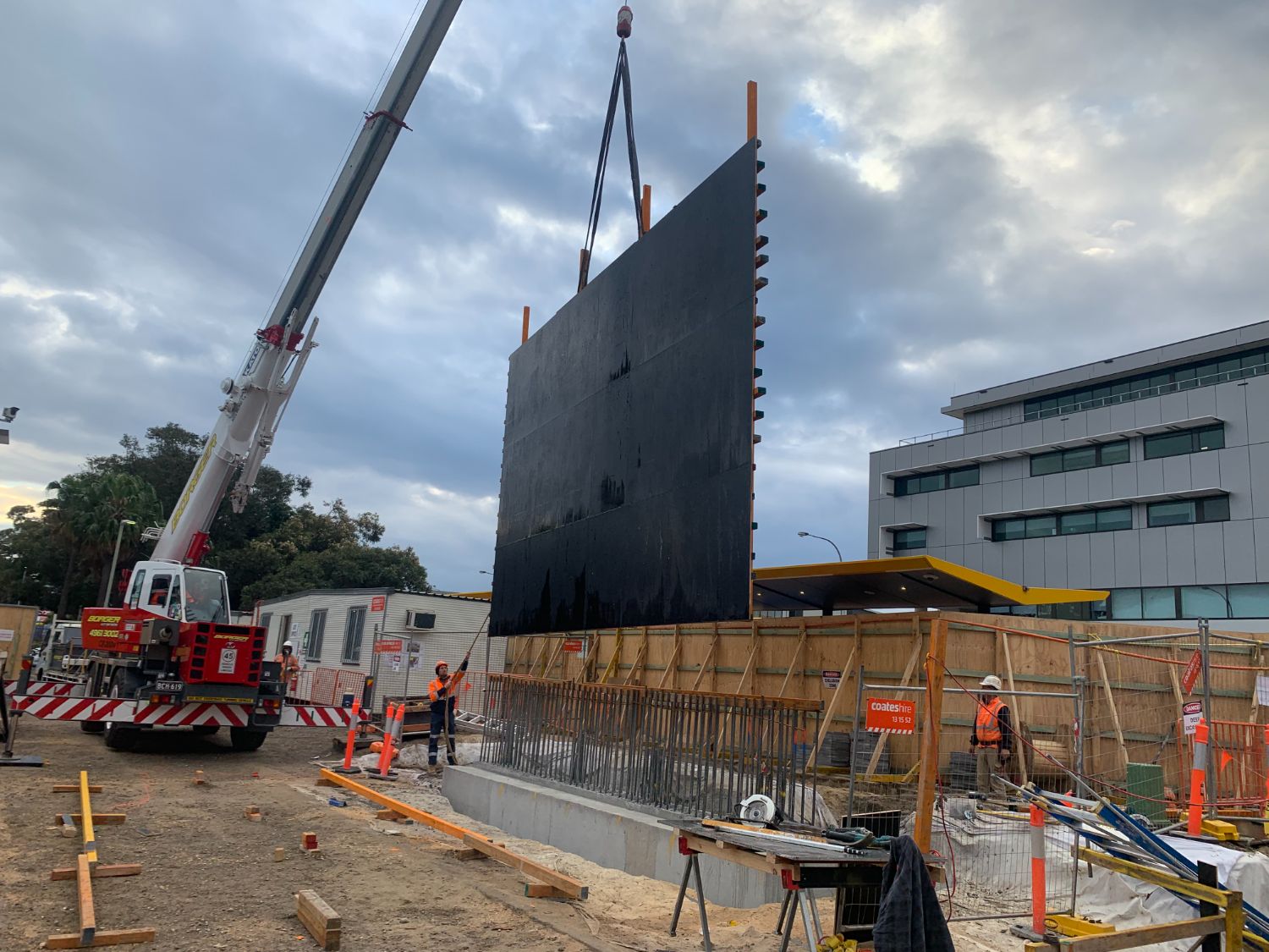 Crane lifting a full-height formwork panel over the starter bars at dusk