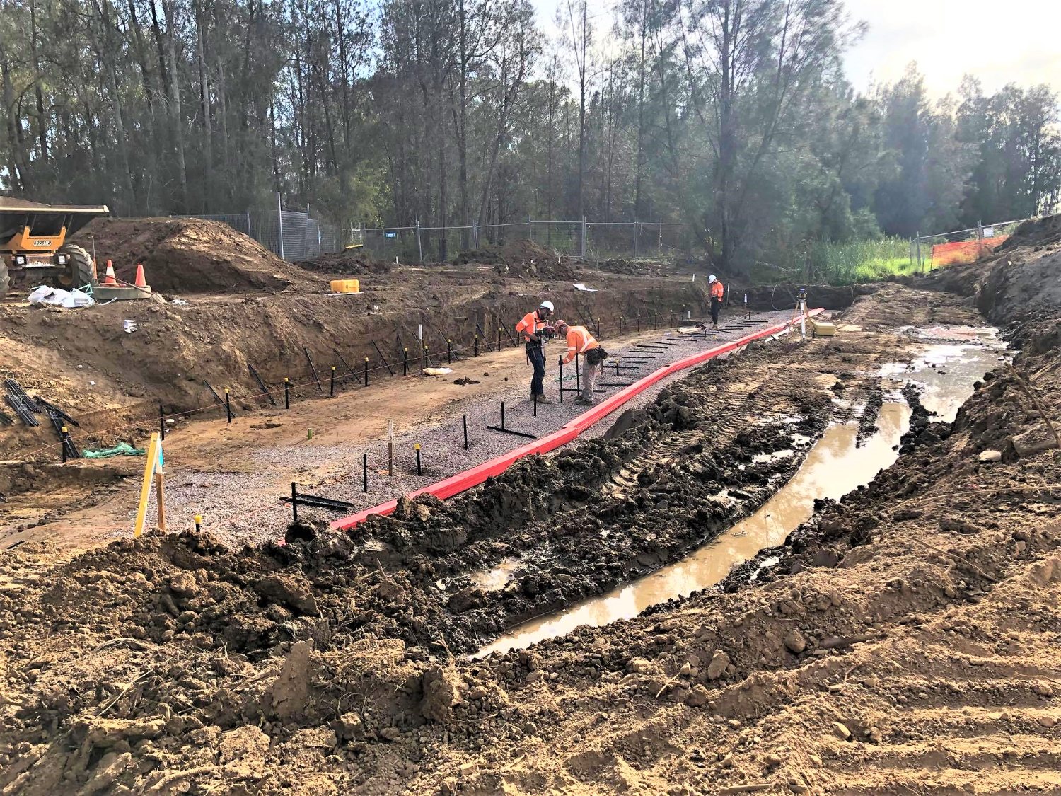 Crew setting out the culvert base within the open excavation beside the creek